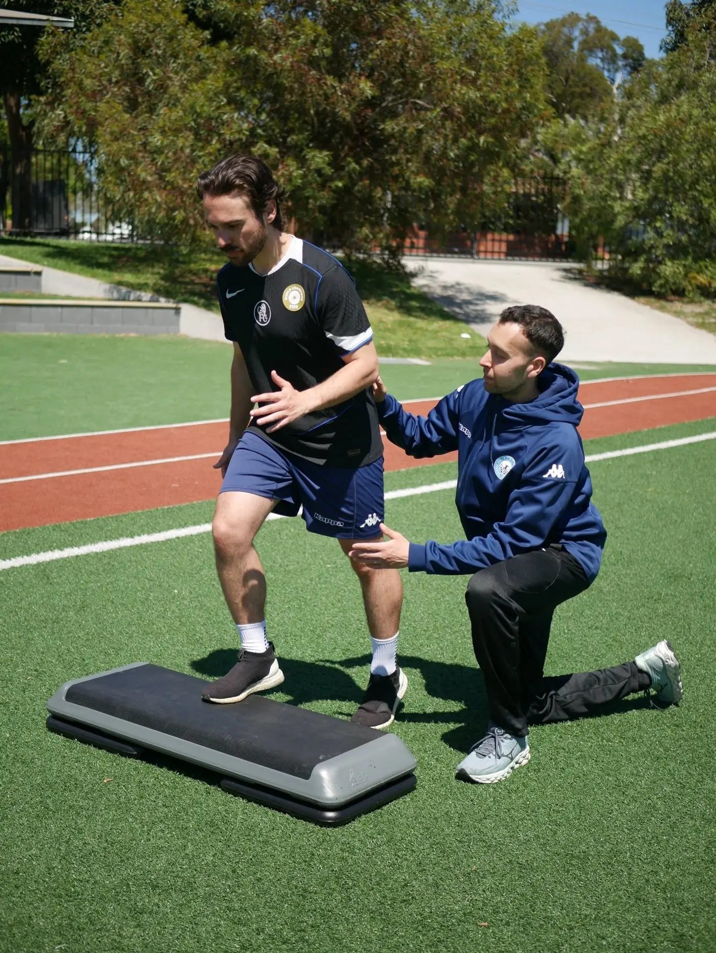 Jake coaching a footballer through a step-up exercise on the track